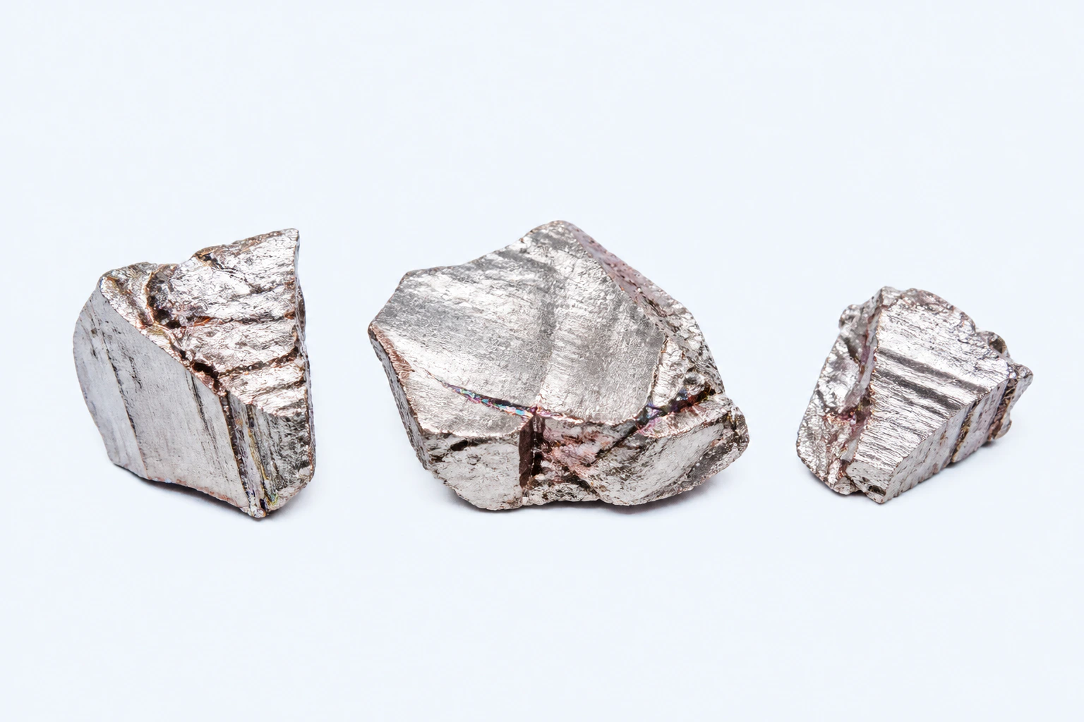 Three elemental bismuth pieces with silvery fracture faces, cool pink undertones, and restrained iridescent ridge tarnish.