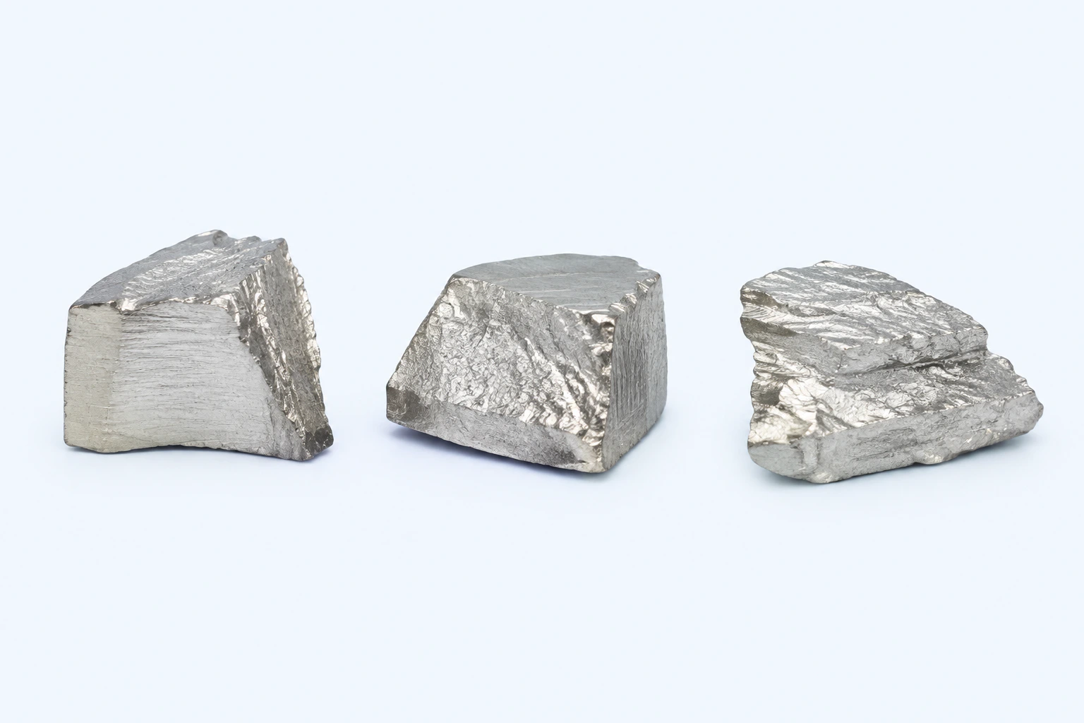 Three elemental titanium specimens with bright silvery-white irregular worked surfaces.