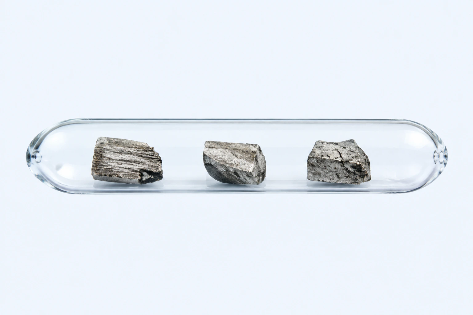 A sealed clear ampoule containing three gray-silver elemental uranium specimens with darker oxidized surfaces.